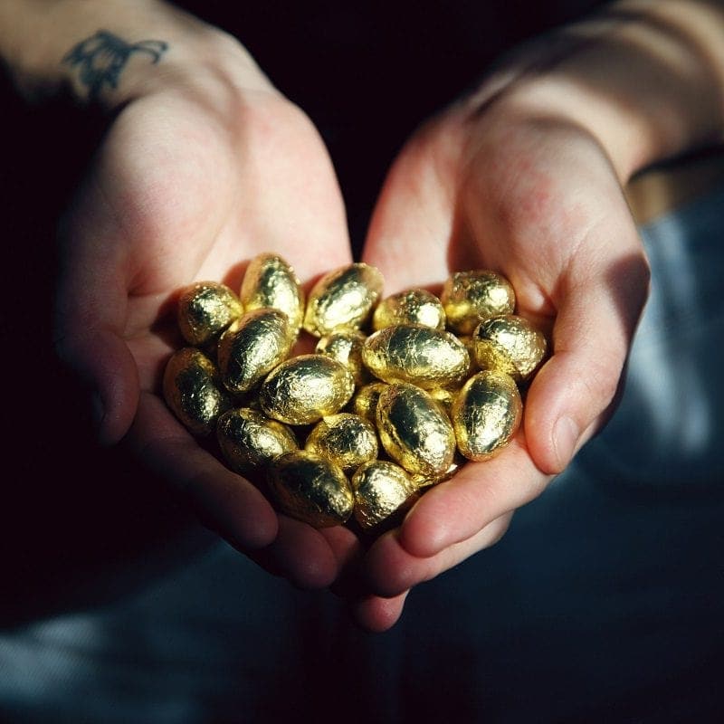 Hands holding a pile of small, oval, gold-wrapped chocolates.