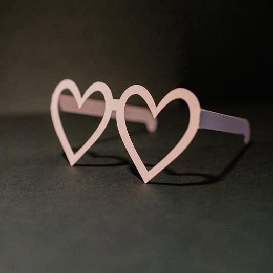 Heart-shaped glasses with pink frames on a dark surface.